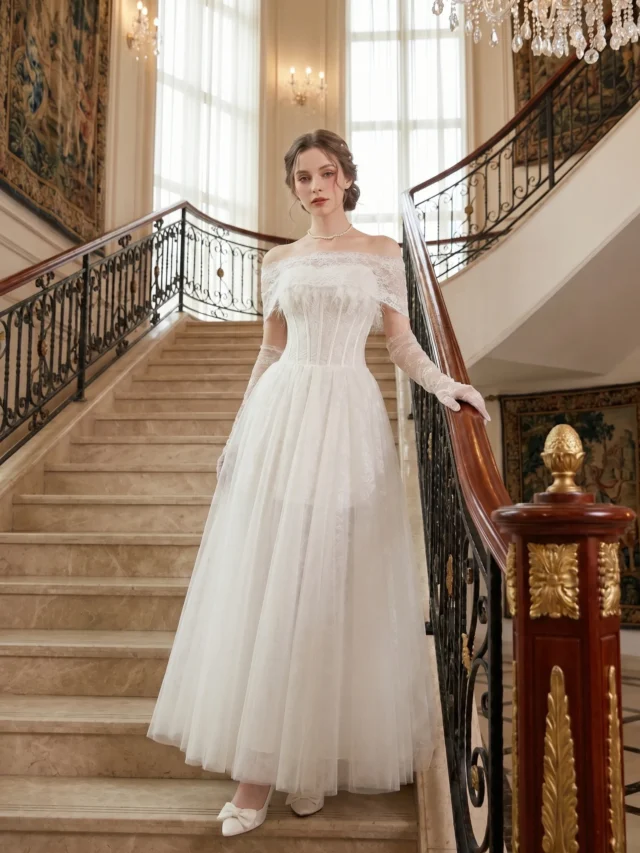 Model wearing Nathalia convertible ivory corset tulle dress featuring an off-shoulder lace cape, structured corset bodice, detachable tulle skirt, and elegant bridal silhouette on a grand staircase.